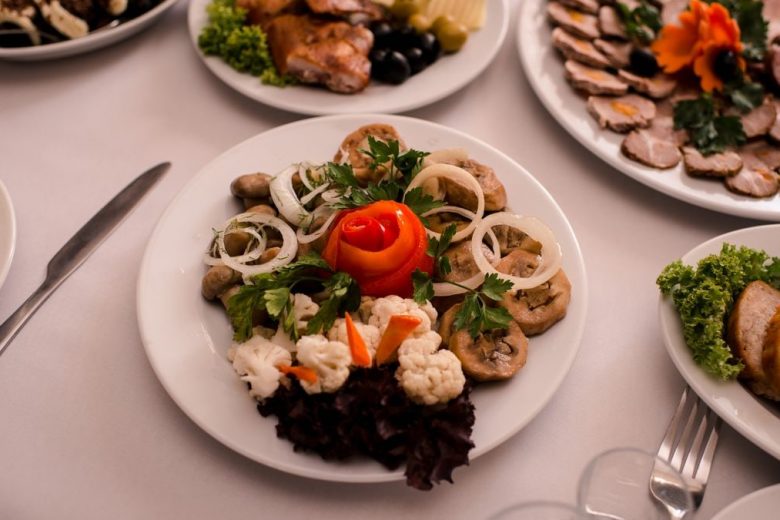Beautifully arranged gourmet plates with meats, cheeses, and garnishes on a white table setting.