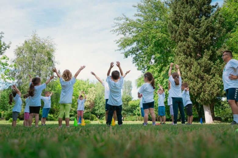 Group of children with instructor doing exercises in a sunny park setting, promoting outdoor activity.